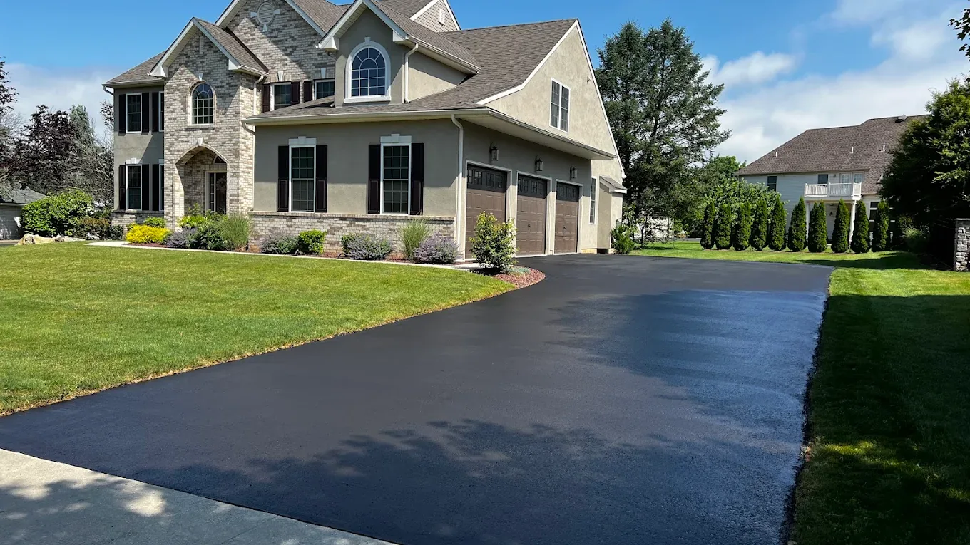 Wide black asphalt driveway sweeping up to a large stone front home